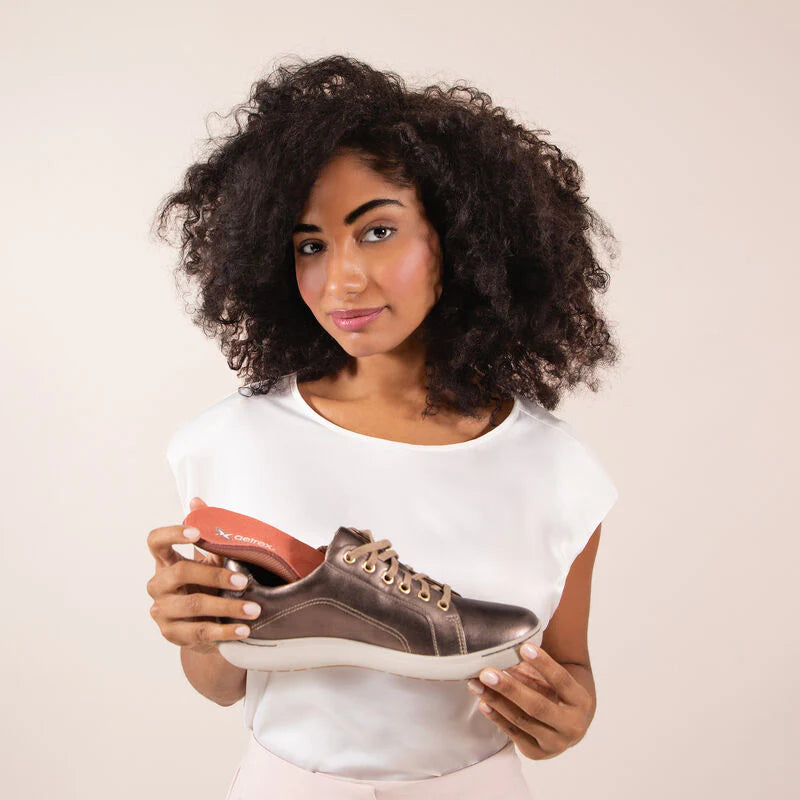 Holding an Aetrex Premium Memory Foam orthotic beside the sneaker it is going into