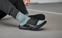 Easing a foot into an OOFOS Sport Flex while seated, showing how far the strap opens