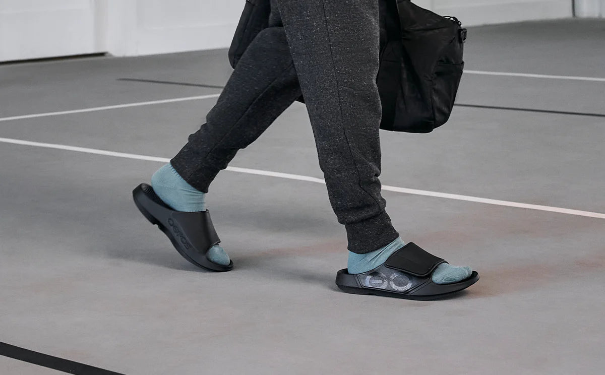 OOFOS Sport Flex worn walking across a gym floor with a duffel bag