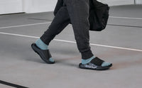 OOFOS Sport Flex worn walking across a gym floor with a duffel bag