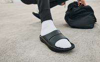 Black OOFOS OOahh Slide worn after a workout, man crouched on concrete beside a gym bag
