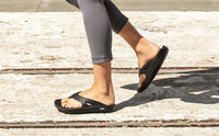 Walking outdoors in black OOFOS OOriginal sandals, side view on the foot